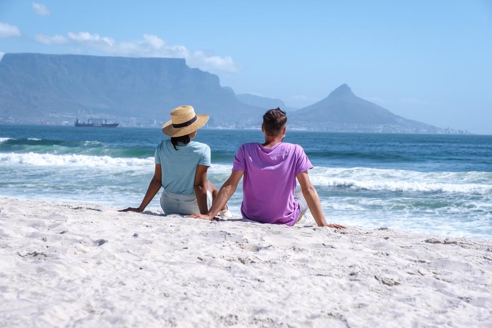 Couple sitting on blouberg beach, Cape Town with table mountain in background